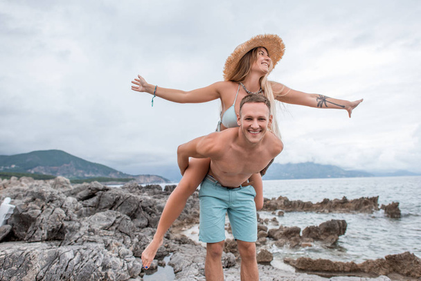 Happy νεαρό ζευγάρι piggybacking και έχοντας διασκέδαση στην βραχώδη παραλία του Μαυροβουνίου  - Φωτογραφία, εικόνα