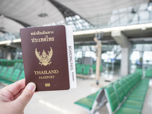 Woman holding Thailand passports and boarding pass in her hand at the airport in the seating gate area - Photo, Image