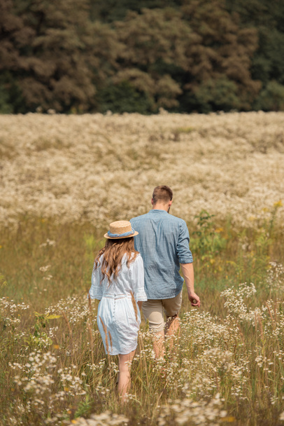 rear view of couple walking in filed with wild flowers around - Foto, Imagem
