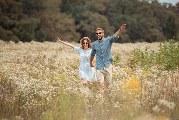 amantes felices tomados de la mano mientras corren en el campo con flores silvestres
 - Foto, Imagen