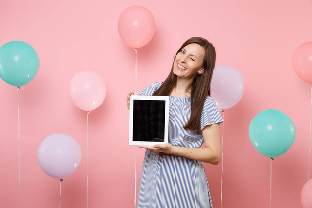 Portret van gelukkig lachende jonge vrouw in blauwe jurk met tablet pc-computer met leeg leeg scherm knippert pastel roze achtergrond met kleurrijke lucht ballonnen. Concept van de partij van verjaardag vakantie - Foto, afbeelding