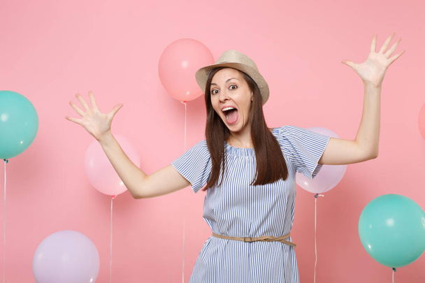 Portrét radost šťastná žena s otevřenou hubou nosí letní slaměný klobouk a modré šaty šíří ruku na růžovém pozadí s barevnými balónu. Oslava narozenin lidí upřímné emoce - Fotografie, Obrázek