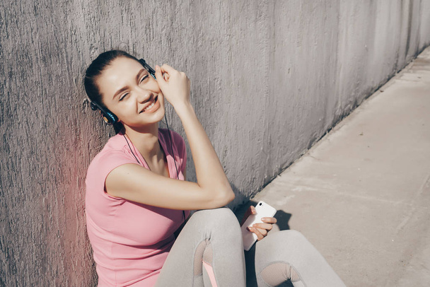 beautiful young girl resting after training in the sun, listening to music on headphones - Foto, afbeelding