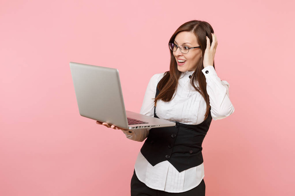 Молодая шокированная успешная деловая женщина, работающая в ноутбуке компьютер цепляясь за голову изолированы на пастельно-розовом фоне. Леди-босс. Концепция карьерного богатства. Копирование места для рекламы
 - Фото, изображение