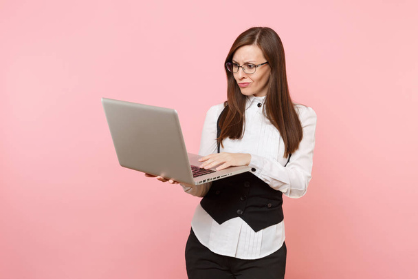 Young irritated dissatisfied business woman in glasses working in laptop pc computer isolated on pastel pink background. Lady boss. Achievement career wealth concept. Copy space for advertisement - Foto, Imagen