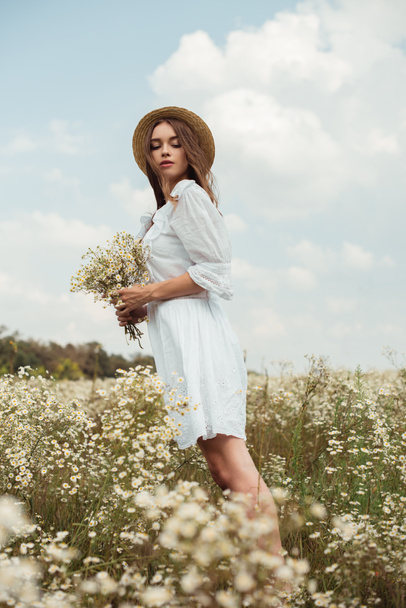 pretty woman in white dress with bouquet of wild camomile flowers on meadow - Fotografie, Obrázek