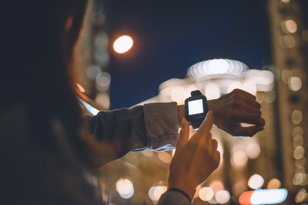 vista parziale della donna con smartwatch al polso e luci notturne della città sullo sfondo
 - Foto, immagini