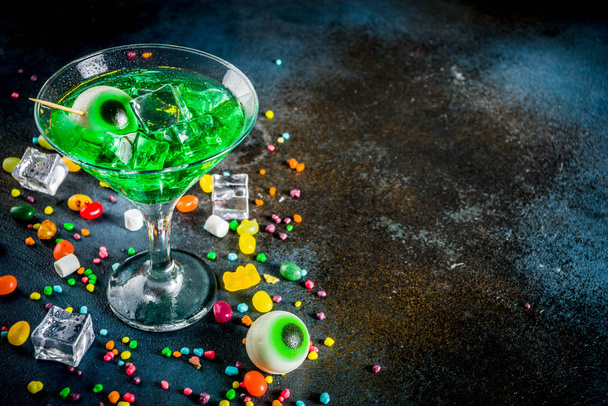 Delizie spettrali per Halloween, un cocktail di martini verde brillante all'arancia con cubetti di ghiaccio e un arredamento di occhi di marshmallow. Su uno sfondo blu scuro, spazio per il testo
 - Foto, immagini