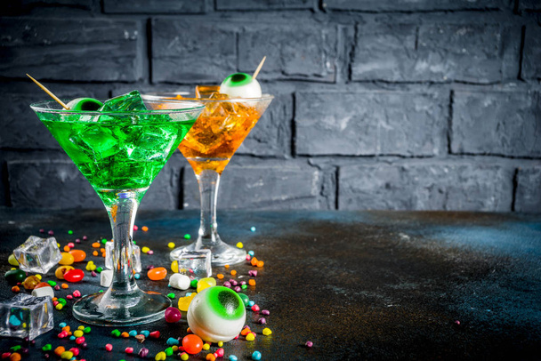 Des friandises effrayantes pour Halloween, un cocktail de martini orange vert vif avec des glaçons et un décor d'yeux de guimauve. Sur fond bleu foncé, espace pour le texte
 - Photo, image