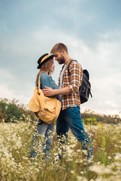 tierna pareja enamorada de las mochilas en el campo de verano con flores silvestres
 - Foto, imagen
