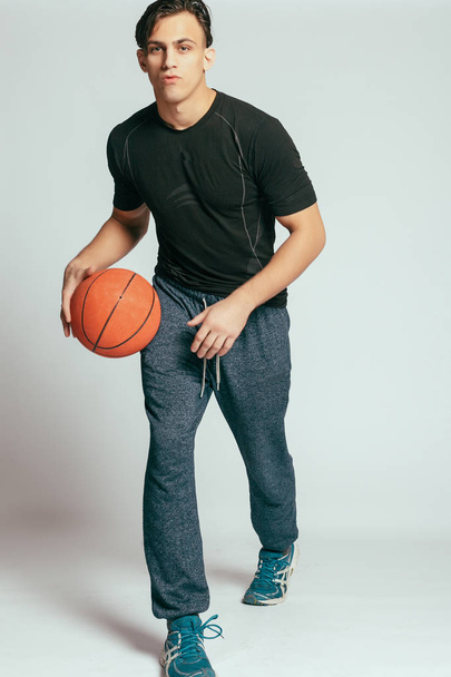 health, people, Sport and lifestyle concept - Real player. Handsome young smiling man carrying a basketball ball and looking at camera while standing against grey background - Photo, image