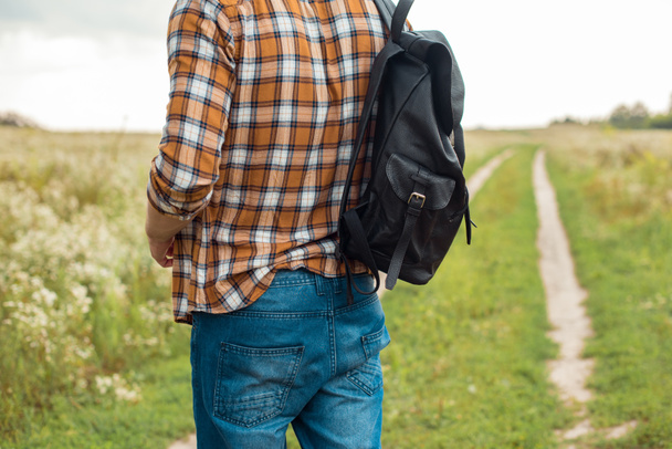 częściowy widok człowieka w dżinsy z czarny skórzany plecak stojący w polu - Zdjęcie, obraz