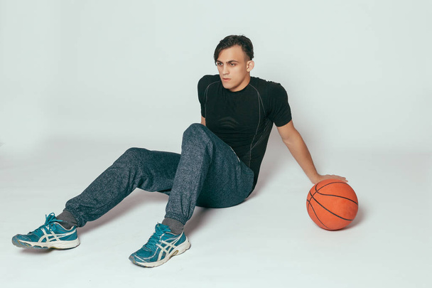 health, people, Sport and lifestyle concept - Real player. Handsome young smiling man carrying a basketball ball and looking at camera while standing against grey background - Foto, Imagem