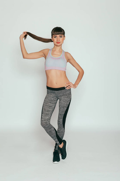 health, people, Sport and lifestyle concept - Young happy fitness girl with sporty body at studio on a gray background. Beautiful fit Girl. Fitness model in gray sportswear. Healthy lifestyle. - Foto, immagini