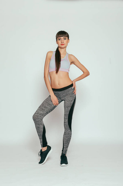 health, people, Sport and lifestyle concept - Young happy fitness girl with sporty body at studio on a gray background. Beautiful fit Girl. Fitness model in gray sportswear. Healthy lifestyle. - Zdjęcie, obraz