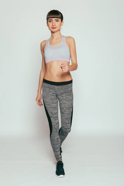 health, people, Sport and lifestyle concept - Young happy fitness girl with sporty body at studio on a gray background. Beautiful fit Girl. Fitness model in gray sportswear. Healthy lifestyle. - Valokuva, kuva