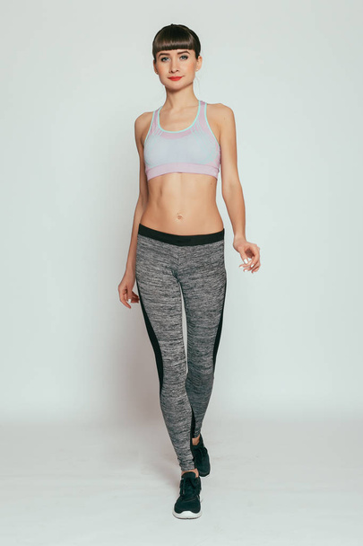 health, people, Sport and lifestyle concept - Young happy fitness girl with sporty body at studio on a gray background. Beautiful fit Girl. Fitness model in gray sportswear. Healthy lifestyle. - Fotó, kép