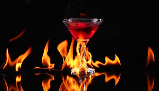 Chilischote in einem Martini-Glas mit Feuer auf schwarzem Hintergrund - Foto, Bild