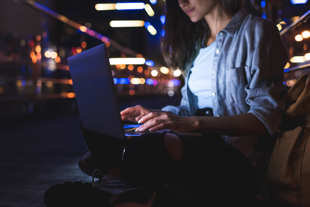vista parcial da mulher usando laptop na rua com luzes da cidade noite no fundo
 - Foto, Imagem