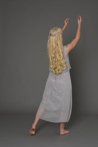 Pełna długość Portret Blondynka dziewczyna ubrana w sukienki i korony. Stojący poza z powrotem do aparatu. studio szary tło. - Zdjęcie, obraz