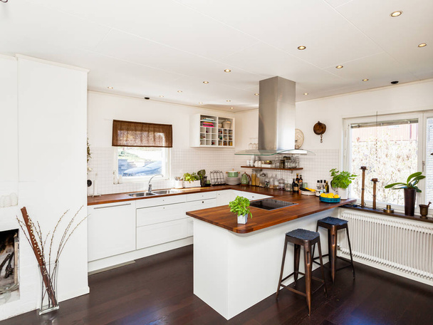 Schicke Küche mit dunklem Boden und weißen Schränken mit Holztischen - Foto, Bild