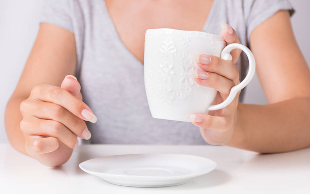 Female hand holding cup of coffee and natural manicure on finger nails. Beauty and drink concept. Close up, selective focus - Photo, Image