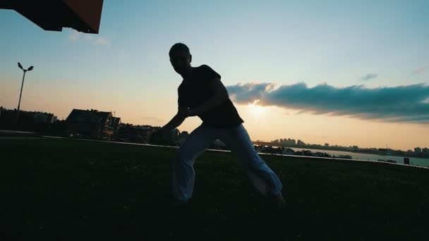 Atletik güçlü adam inanılmaz bir numara capoeira dövüş sanatı günbatımında gösterir - Video, Çekim