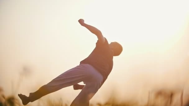 Capoeira, dans atletik adam bir güzel yaz gün batımı arka plan üzerinde zor bir atlama gerçekleştirir - Video, Çekim