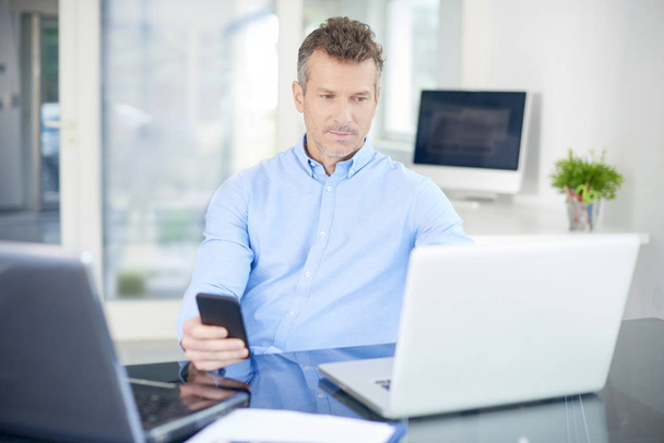 Portrait of middle aged businessman wearing shirt while sitting at the office and working. Professional man using his mobile and text messaging while working on laptops. - 写真・画像