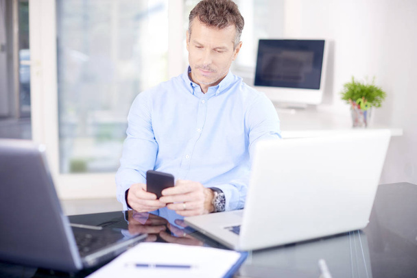 Portrait of thinking businessman wearing shirt while sitting at the office and working. Professional man using his mobile and text messaging while working on laptops. - 写真・画像