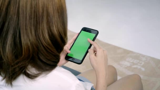 Jovem mulher asiática usando dispositivo de smartphone preto com tela verde. Mulher asiática móvel, rolando páginas enquanto sentado no sofá na sala de estar. Chave Chroma
. - Filmagem, Vídeo