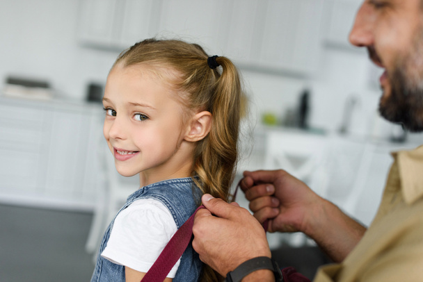 partial view of father helping daughter to wear backpack at home, back to school concept - Photo, Image