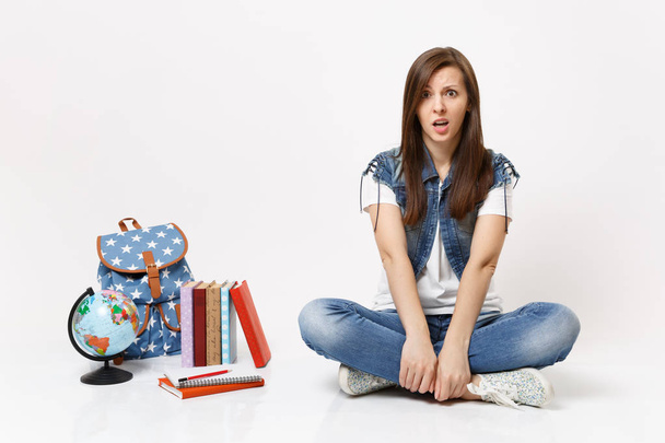 Portrait of casual shocked concerned upset woman student in denim clothes sitting near globe, backpack, school books isolated on white background. Education in high school university college concept - Photo, Image
