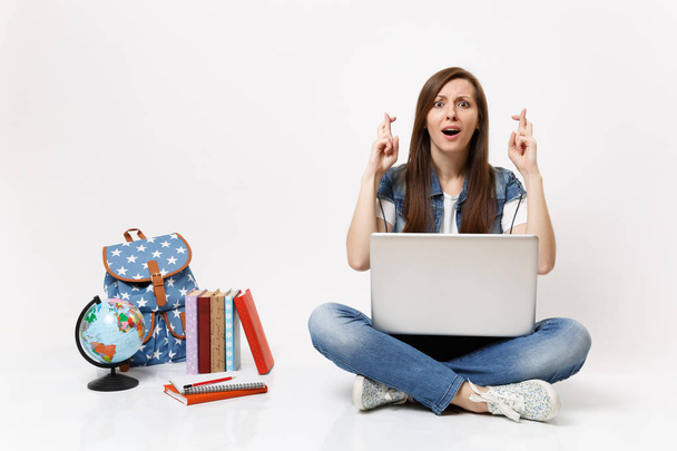 Nuori nainen opiskelija pidä kannettava tietokone odottaa erityistä hetkeä pitää sormet ristissä lähellä maailmaa reppu koulun kirjoja eristetty valkoisella taustalla. Koulutus lukion yliopisto college
 - Valokuva, kuva