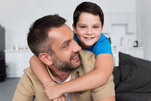 portrait of smiling boy hugging father and looking at camera at home - Foto, Imagen