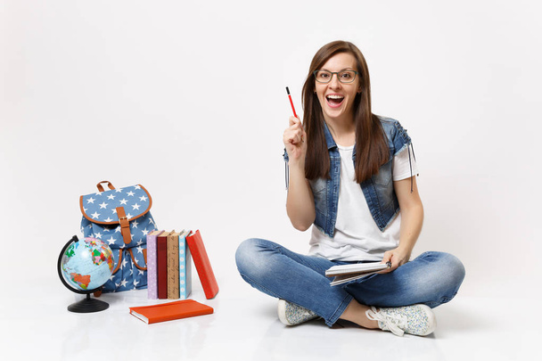 Młodych zdziwiony student kobieta oświecony z nową myślą wskazując ołówek się gospodarstwa notebook w pobliżu globe plecak, podręczniki szkolne, izolowana na białym tle. Edukacja w liceum university college - Zdjęcie, obraz