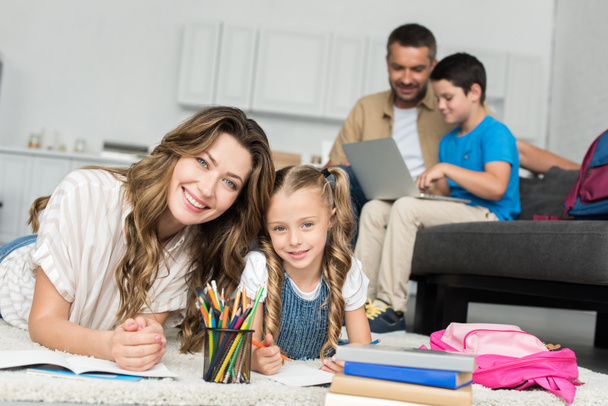 вибірковий фокус усміхненої матері та дочки роблять домашнє завдання, а батько та син використовують ноутбук на дивані вдома
 - Фото, зображення