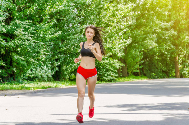 Tyttö punaisissa shortseissa juoksee puistossa.
 - Valokuva, kuva