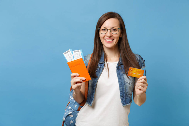 青の背景に分離されたパスポート搭乗券チケット クレジット カードを保持しているバックパックとメガネの若い笑顔女性学生。海外の大学での教育。空気旅行飛行の概念 - 写真・画像