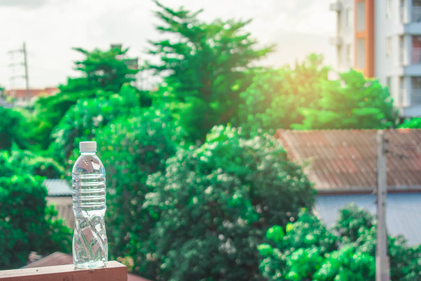 Butelka wody wykonane z tworzywa sztucznego na niebie z domu i drzewa bokeh zamazane - Zdjęcie, obraz