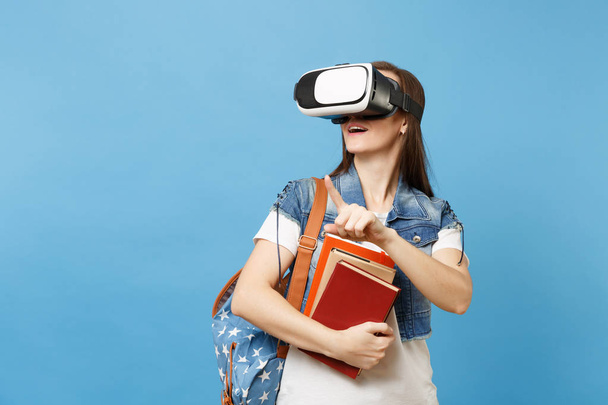 Fiatal nő diák virtuális valóság szemüveg tartsa könyvek érint valami nyomja a gombot, mint lebegő kék háttér elszigetelt virtuális képernyő mutatva. Az iskola egyetemi főiskolai oktatás - Fotó, kép