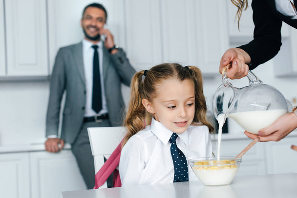 selective focus of kid in school uniform at table with breakfast and mother pouring milk into bowl with crunches at home, back to school concept - Foto, Bild