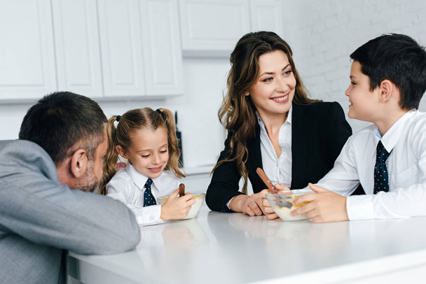 family in suits and school uniform having breakfast in kitchen together - Foto, Imagem
