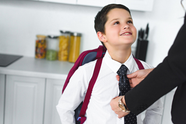 částečný pohled matky v obleku vázání synové kravatu v kuchyni doma, zpět do koncepce školy - Fotografie, Obrázek
