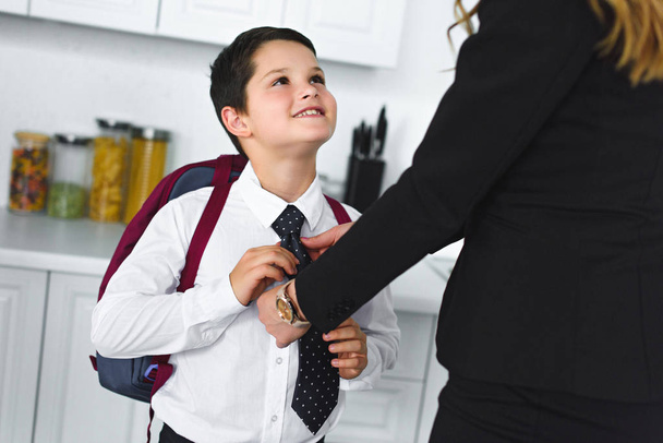 partial view of mother in suit and son in school uniform with backpack in kitchen at home, back to school concept - Photo, Image