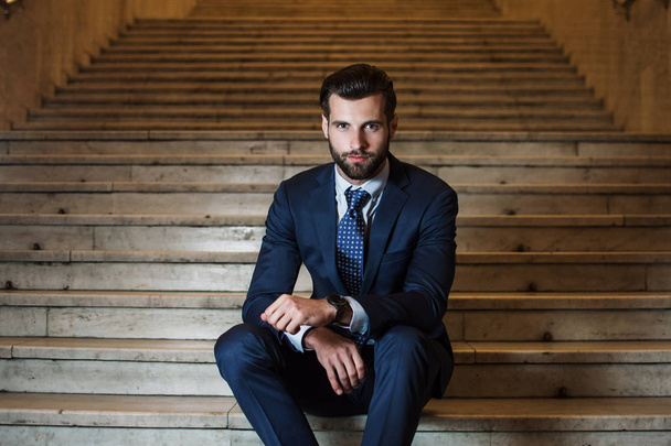 Un hombre de negocios con estilo. Retrato de un joven guapo mirando la cámara mientras está sentado en las escaleras al aire libre
 - Foto, Imagen