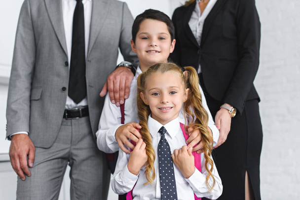 partial view of smiling kids in school uniform and parents in suits at home - Foto, Bild