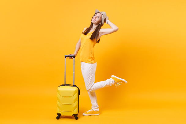 Mujer turista viajera en ropa casual de verano, sombrero con maleta aislada sobre fondo amarillo anaranjado. Pasajera viajando al extranjero para viajar los fines de semana. Concepto de vuelo aéreo
 - Foto, Imagen