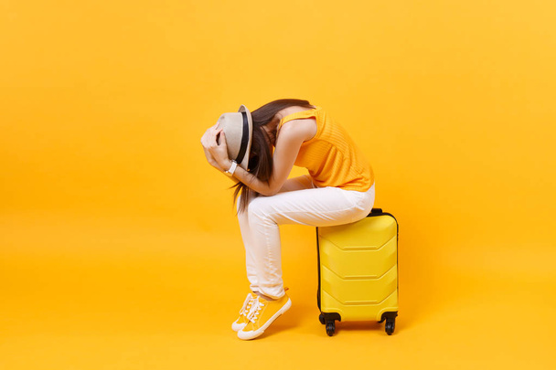 夏のカジュアルな服で動揺観光客の女性は黄色のオレンジの背景に隔離された頭の上に手を置くスーツケースに座っている。週末旅行に海外旅行する女性。航空旅のコンセプト - 写真・画像