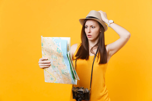 Puzzled traveler tourist woman in summer casual clothes, hat lokking on city map isolated on yellow background. Female traveling abroad to travel on weekends getaway. Air flight journey concept - Zdjęcie, obraz